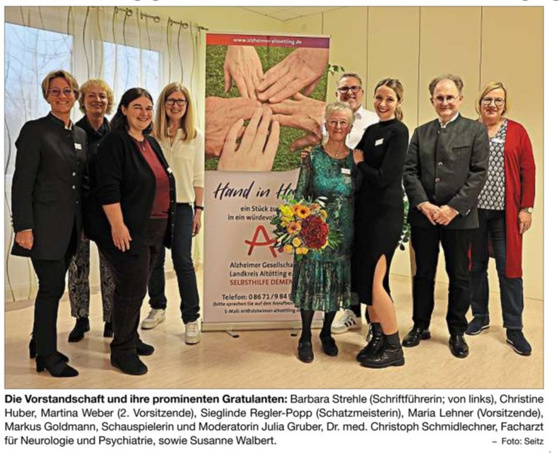 Bild vom Jubiläum. Vorstand des Vereines und Frau Gruber (Moderation) sowie Herr Dr. Schmidlechner vor dem Aufsteller der Alzheimer Gesellschaft Landkreis Altötting e. V. vom 13.11.2024