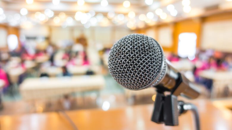 Schwarzes Mikrofon im Fokus - dahinter verschwommener hell erleuchteter Raum mit Tischen und Stühlen. Quelle Bild: de.freepic.com/fotos-kostenlos - von janoon028
